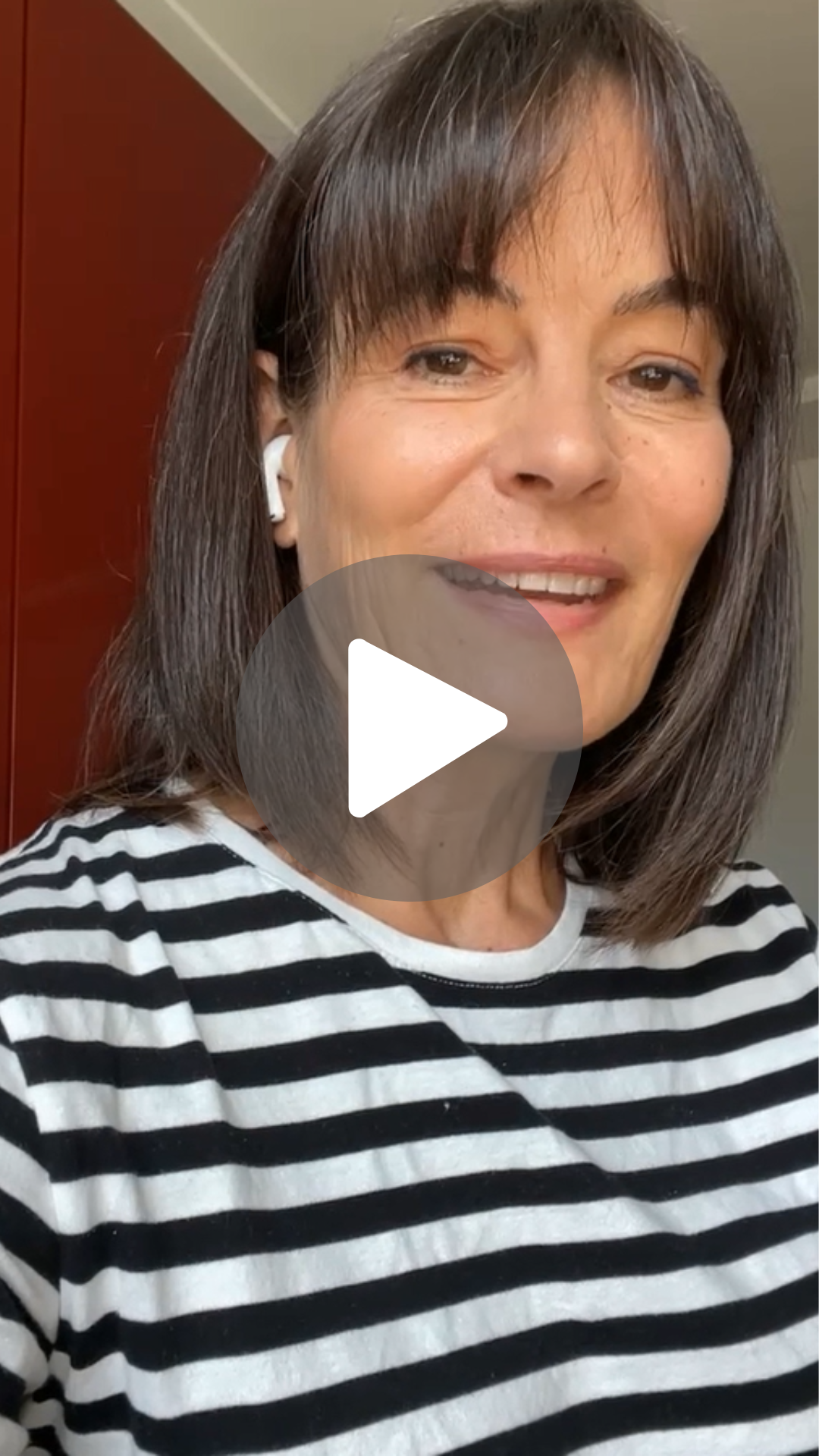 Hanna Jensen raidallisessa paidassa, käyttää korvakuulokkeita, hymyilee kameralle