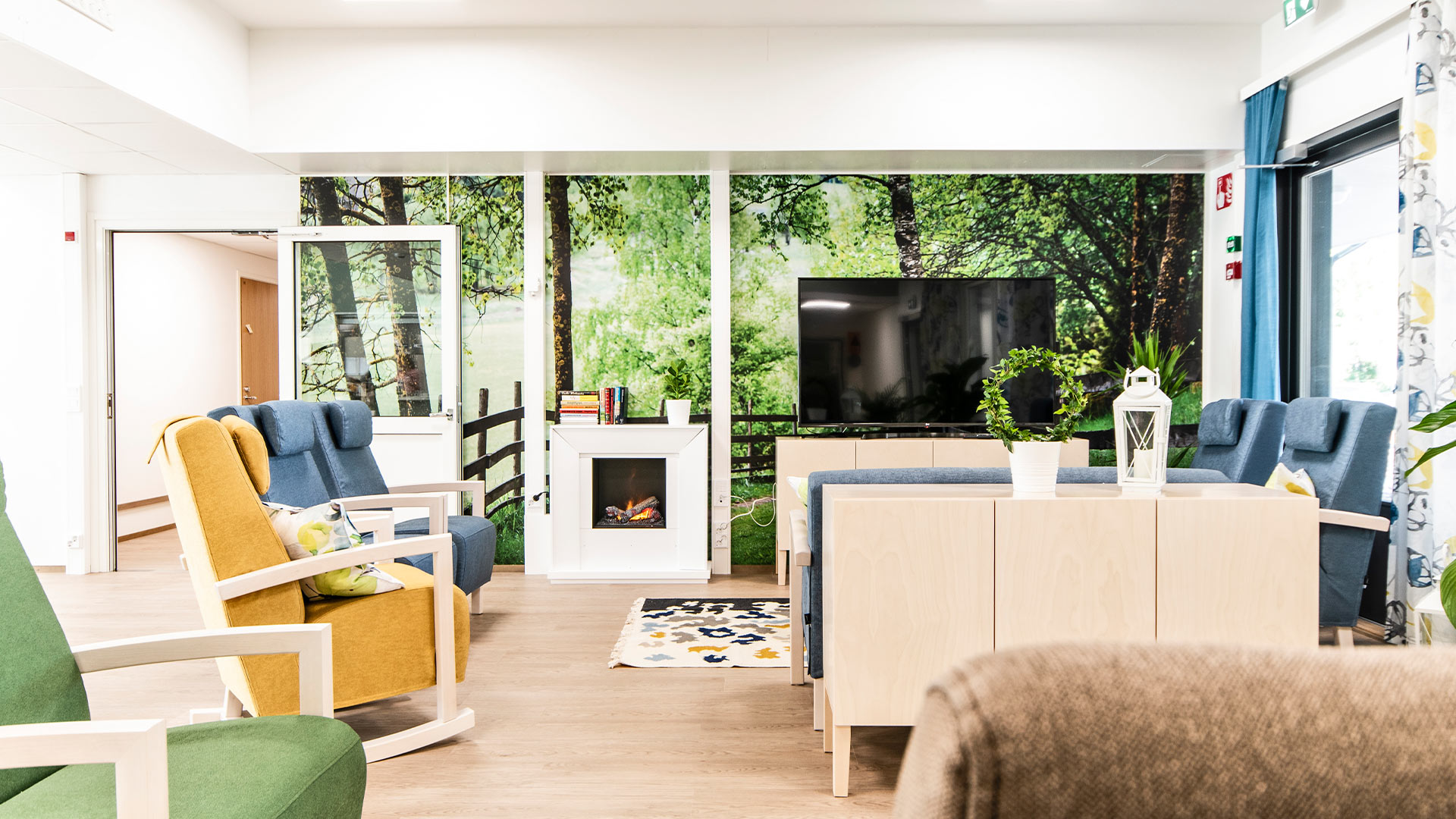 Moderni olohuone, jossa on monivärisiä nojatuoleja, televisio, vihreä metsätapetti ja koriste-esineitä