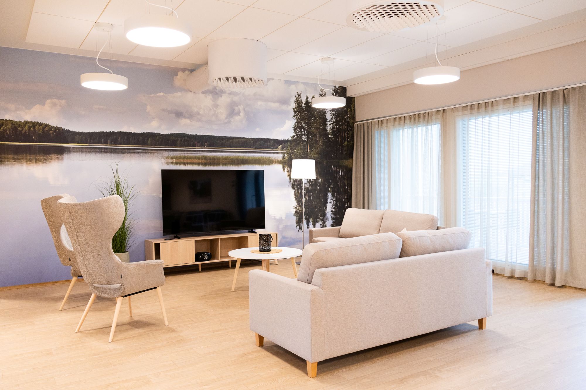 Kirkkaasti valaistu olohuone televisiolla, sohvalla ja maisematapetilla