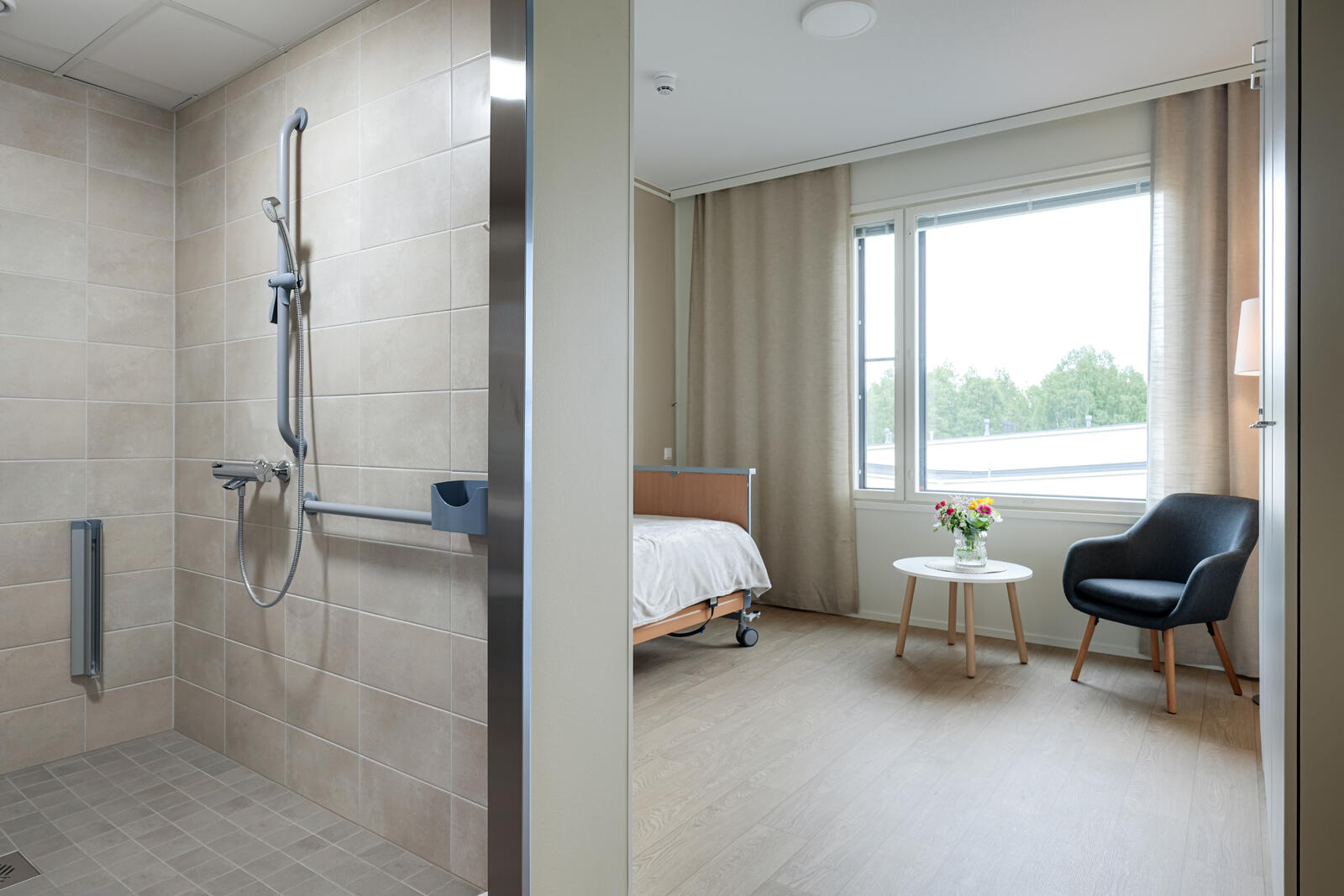 Attendo Revontulen asukashuone. Näkyvillä WC-tiloja, ikkuna, yöpöytä ja nojatuoli.