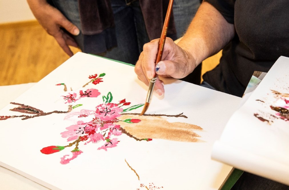 henkilö maalaa vesiväreillä punaista kukka-aihetta