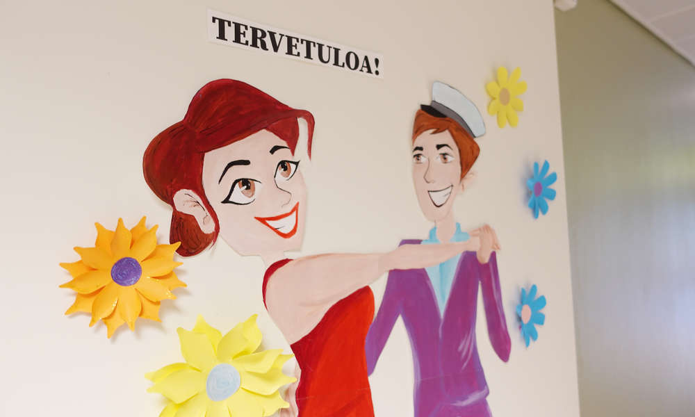 Kuva seinällä olevasta Tervetuloa-julisteesta, jossa kaksi henkilöä tanssii keskenään