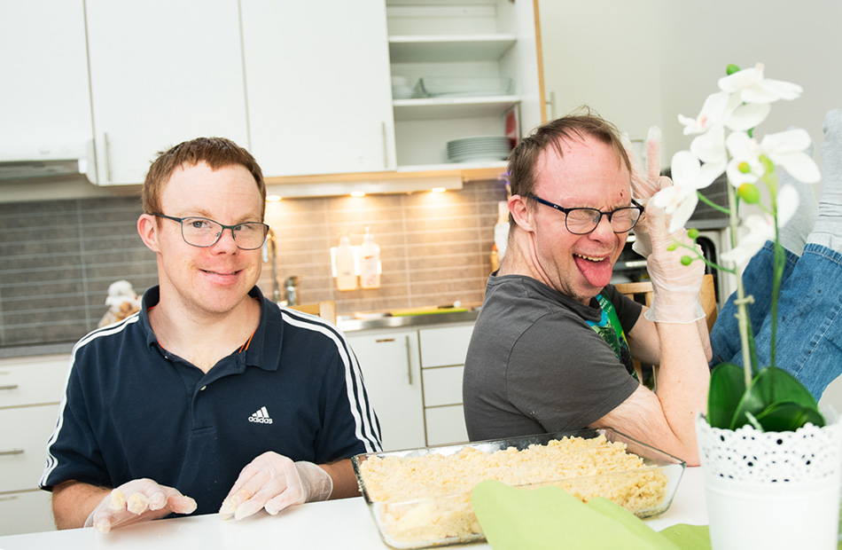 Kaksi kehitysvammaista henkilöä hymyilee kameralle keittiössä