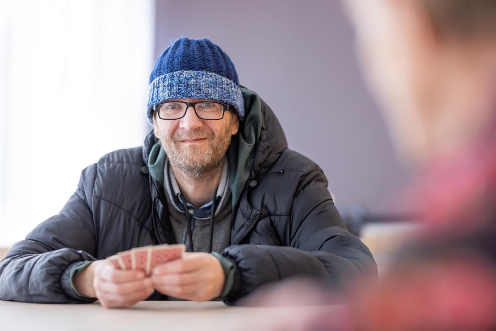 Mies pipo päässä pöydän ääressä pelaamassa korttia toisen henkilön kanssa