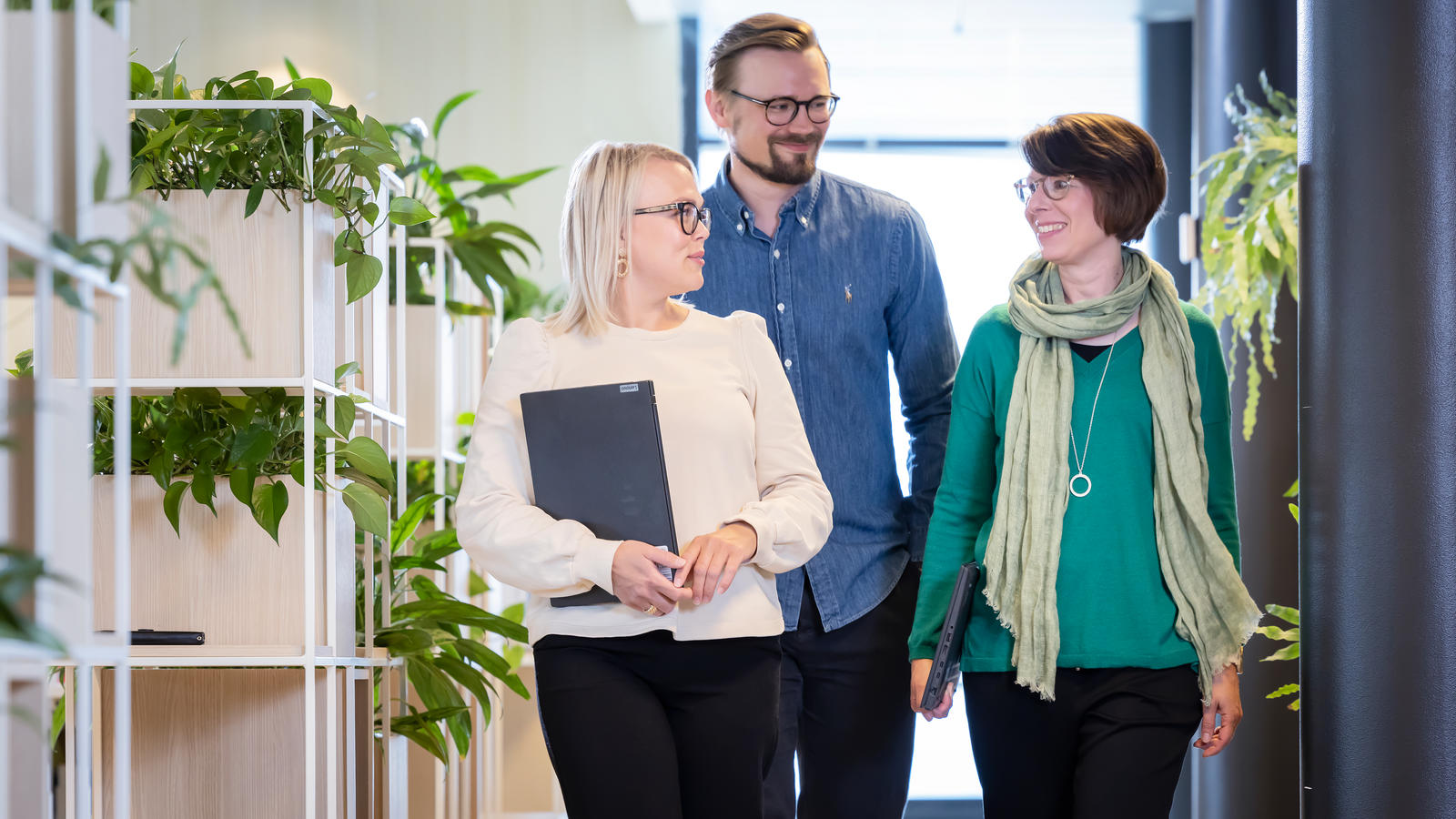 Kaksi naista ja yksi mies kulkee toimiston käytävällä vierekkäin ja keskustelee keskenään