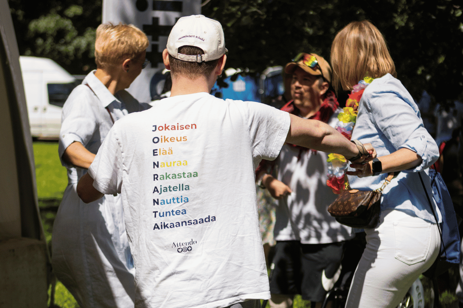 Attendolaisen valkoisen paidan sel&auml;ss&auml; sateenkaariv&auml;rein teksti: Jokaisen Oikeus El&auml;&auml; Nauraa Rakastaa Ajatella Nauttia Tuntea Aikaansaada. Taustalla ihmisi&auml; Pride-tapahtumassa.
