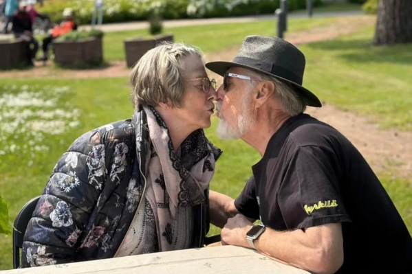 Kuvassa asukas ja läheinen, pariskunta, suukottavat toisiaan kesäisessä maisemassa.