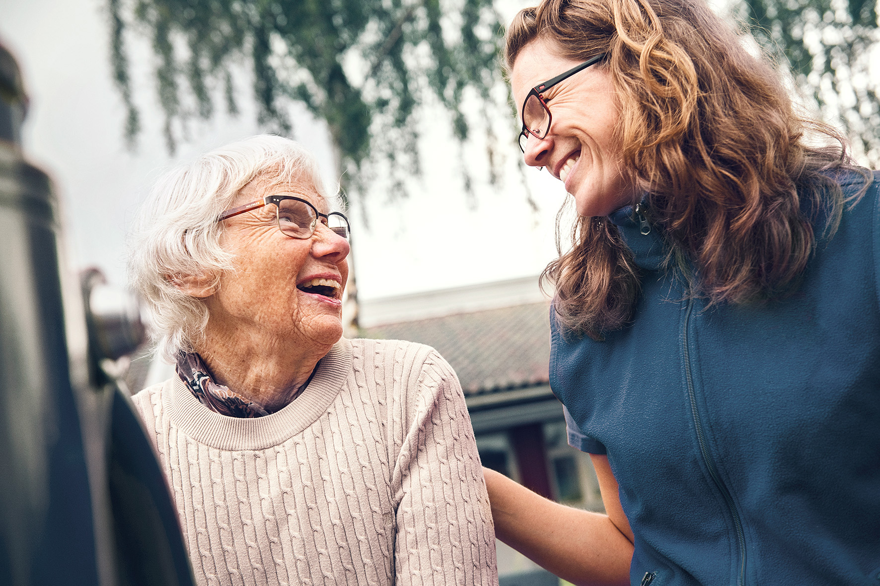 Hoitaja ja hoivakodin asukas katsovat toisiaan ja hymyilevät hoivakodin pihalla
