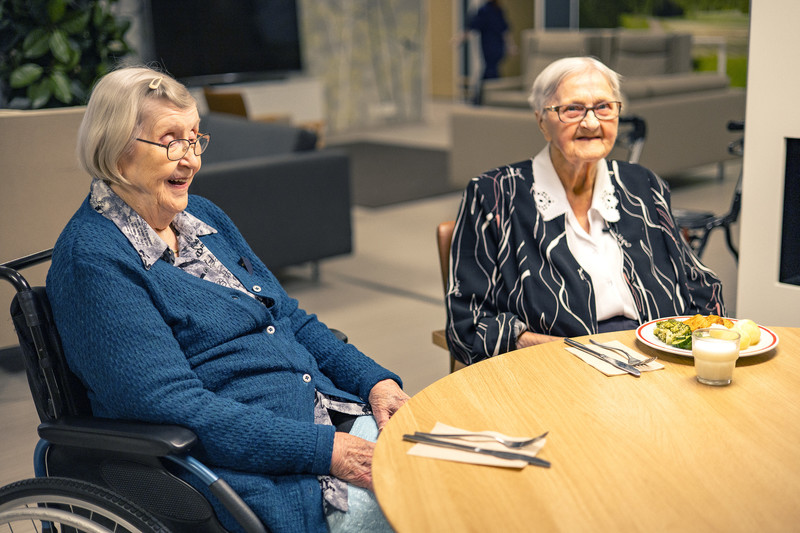 Kaksi henkilöä hoivakodissa ruokapöydässä odottamassa ruokaa